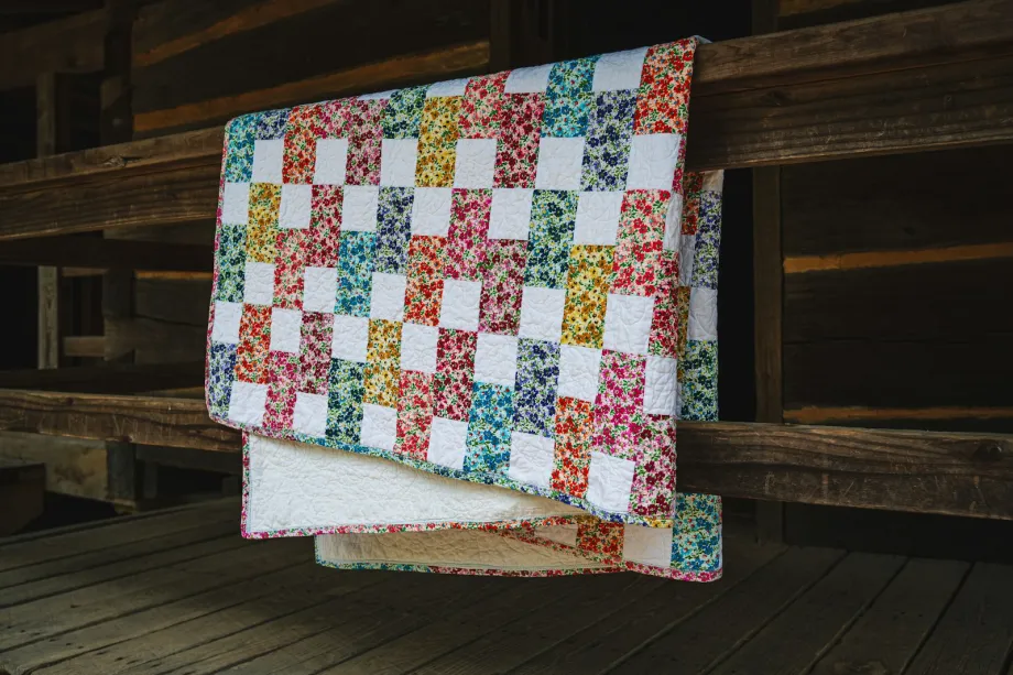 Quilt of floral print and white squares in a diagonal checkerboard, draped over a wooden railing