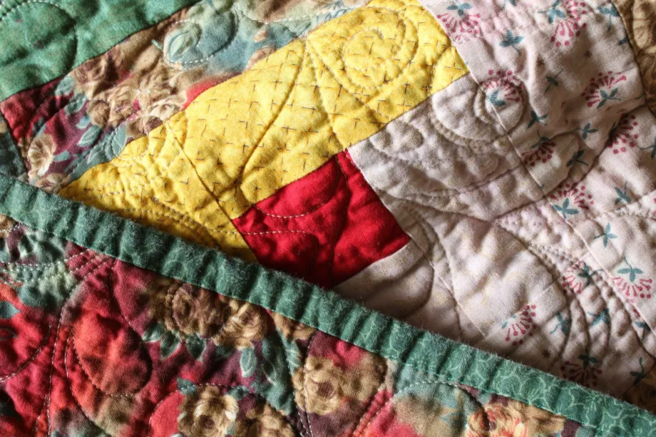Close-up of a hand-quilted quilt in red, yellow and floral prints with curved quilting stitches