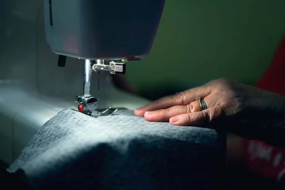 Hand guiding gray fabric under the presser foot of a sewing machine