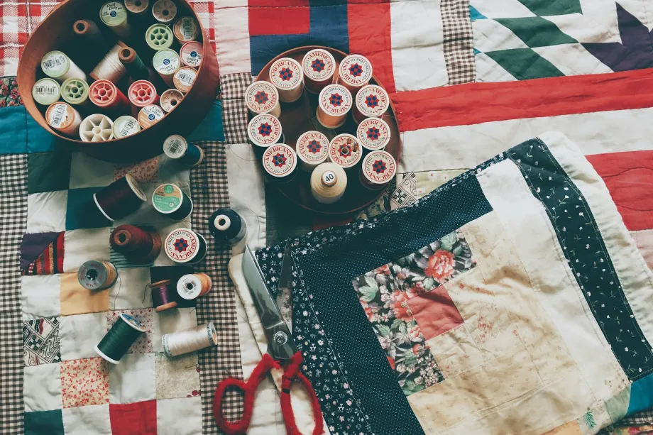 Patchwork quilts on a table with spools of thread, red-handled scissors and a log cabin block