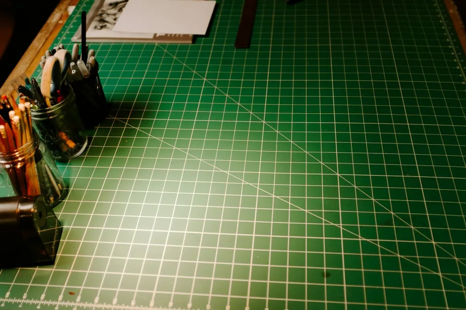 Green self-healing cutting mat with a printed grid beside jars of pencils and scissors